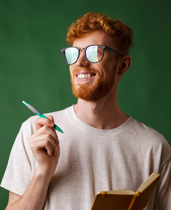 A man in glasses is holding a notebook and a pen.