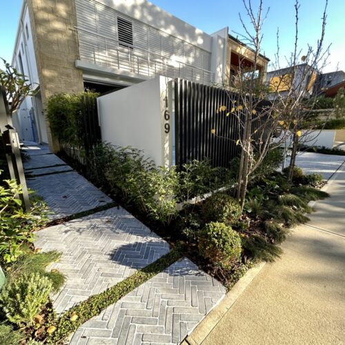 A walkway leading to a house with plants and shrubs.