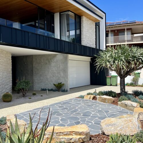 A modern home with a stone driveway and cactus.