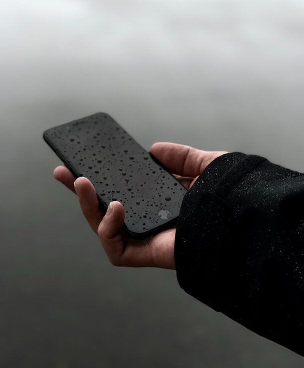 A person holding a black phone with rain drops on it.