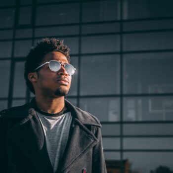 A black man wearing sunglasses in front of a building.